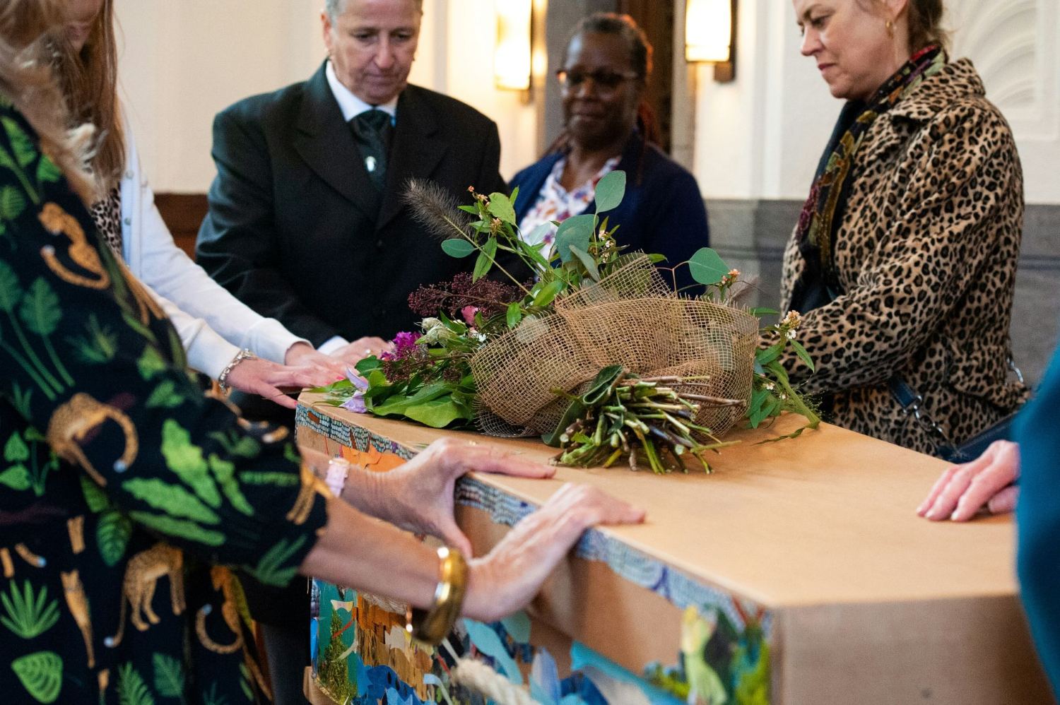 Funeral directors and family surrounding a cardboard coffin at a funeral service